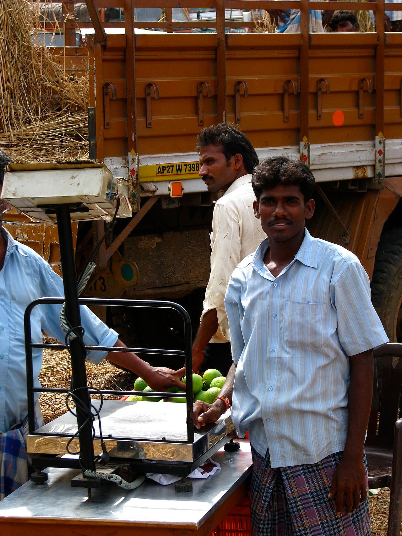 Traders weighing fruit beside a loaded truck at a wholesale market